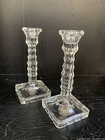 Pair of clear EAPG candlesticks with textured geometric stems and square bases.