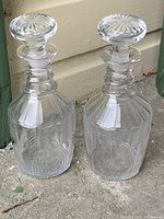 Pair of antique Victorian glass decanters side by side showing original stoppers and detailed faceted glass designs.