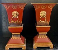 Pair of red tapered planter urns with gold lion's head ring detail on the front and ornate gold floral and leaf painted accents.