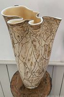 Photo of a large decorative glass vase with an irregular wavy edge and crackle patterned surface in cream and brown tones, standing on a wooden surface against a white background.