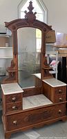 Full view of a very large antique wooden dresser with marble tops and tall arched mirror attached, showing detailed wood carving and ornate hardware.