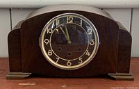 Front view of wooden Art Deco mantel clock showing curved top, stepped sides and round dial
