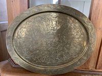 Front view of vintage brass tray showing intricate etched floral and scroll patterns on large oval surface