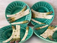 Four green slip glazed Majolica asparagus plates with molded white asparagus decoration on top. Plates are oval and measure about 9 inches wide.