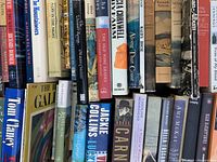 Photo showing the spines of various vintage and first edition books including titles like 'The Old Vine Shards,' 'The Gate,' 'Vices of My Blood,' and works by authors Jackie Collins, Michael Crichton, and P.G. Wodehouse.