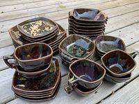 Wide view of the full dish set showing stacked plates, bowls, and cups in brown and green glaze on a wooden surface.