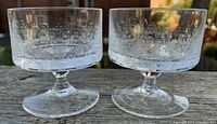 Pair of small Rosenthal coupe glasses with etched romance motif shown on wooden surface outdoors in daylight.