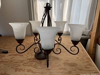 Chandelier with five curved arms and frosted glass shades on each arm, showing entire fixture.