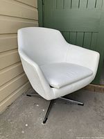 View of the white leatherette swivel chair with chrome base angled to the left side. Chair shows egg style with padded armrests and seat cushion.