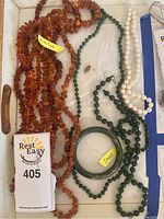Top view of the lot showing amber chip necklaces, green jade bead necklaces, a jade bangle bracelet, and a pearl strand without clasp in a white tray.