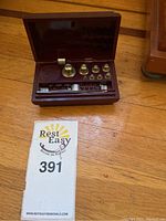 Full view of the apothecary weight set with case open on wood floor displaying weights and balance beam.