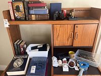 Wide view of wooden shelf containing books, office supplies, binoculars, speaker, and blood pressure monitor.