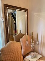 View showing glass candelabra with gold candles placed on a chair in front of large framed mirror reflecting room interior.