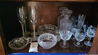 Photo of assorted crystal and glass stemware including two decanters, various bowls, trays, and cocktail glasses with etched patterns.