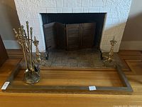 Overall view of fireplace border bar positioned in front of fireplace with brass tools and candlesticks inside the border.