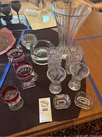 View of full set including tall clear cut crystal vase, ashtrays, candle holders and ruby cut glass pieces on black cloth