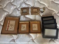 Overview of all artwork and frames on mattress surface including the three Japanese framed bamboo art pieces, seven black frames, and two gold decorative mini frames.