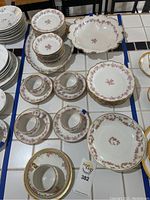 Overview photo showing the full limoges china set arranged on a tiled surface, displaying plates, cups, saucers, and the large serving bowl. Several pieces have blue tape marking chips.