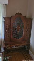 Full front view of carved wood cabinet with glass fretwork door and bracket base