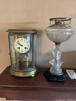 Front view showing both the brass cylinder clock and figural oil lamp on tabletop