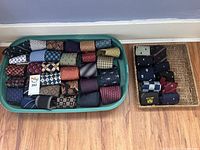 Two trays filled with rolled neck ties showing assorted patterns and colors arranged on floor against wall.