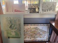 Photo showing several framed art prints on a shelf including Raoul Dufy poster and illustrated map poster