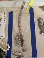 Full view of silver necklace and three unique pins arranged on a tray with blue tape markings and label.