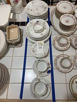 Full view of multiple Theo Haviland porcelain dinnerware pieces including cups, plates, and bowls arranged on a table. Some chips marked with blue tape.