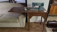 Full view of wooden sewing table with sewing machine and foot pedal visible, positioned next to a couch.