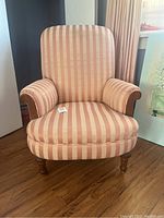 Front view of vintage striped arm chair showing padded seat, curved arms with wooden accents, and fabric upholstery with vertical stripes in beige and pink shades.