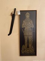 Full view of the framed brass rubbing and mounted machete on wall.