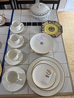 Full view of tea cups, saucers, plates, serving and decorative dishes arranged on tiled surface.