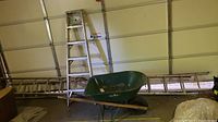 Wide view showing wheelbarrow in front and three ladders leaning against the wall in the background.