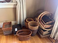 Overview of multiple stacks of wicker baskets of varying sizes and shapes arranged near wall and curtain.