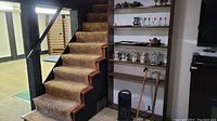 View of stairway near black vertical space heater and wooden shelving with assorted barware and accessories