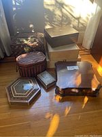 Seven assorted wooden boxes arranged on a wood floor near a window, showing different shapes and finishes.