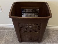 Photo of a rectangular dark brown plastic laundry hamper bin showing ventilation holes on the sides and the top rim with two lid notches.