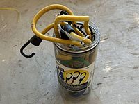 Clear container holding 13 assorted heavy duty bungee cords with plastic-coated metal hooks on each end, in various colors and sizes, resting on a concrete floor.