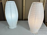 Two white oval paper lamps on metal stands illuminated from inside showing ribbed paper texture.