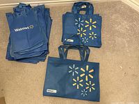 Photo showing multiple blue reusable shopping bags from Walmart in two distinct designs and various sizes stacked on floor.