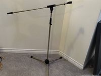 Photo of an adjustable microphone stand showing the vertical pole, horizontal boom arm, and tripod base with three legs.