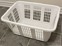 White plastic laundry basket with ventilation holes on tile floor.