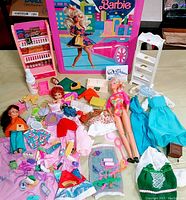 Overview of Barbie dolls, clothes, shoes and accessories spread out in front of Barbie pink trunk case