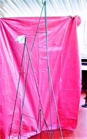 Three green metal tripod wreath holder stands of varying heights positioned against a pink backdrop, showing full height and structure.