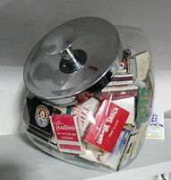 Glass candy jar with stainless steel lid filled with various vintage matchbooks.