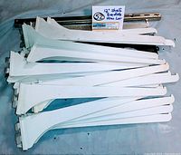 Stack of white single track 12-inch metal shelf brackets along with some silver pieces in the back