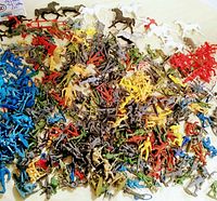 Top-down image showing a large assortment of vintage plastic toy soldiers, horses, cowboys, Indians in multiple colors and poses spread out on a flat surface.