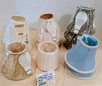 Photo of 7 mini bell lamp shades taped to a white background, colors include tan, brown, white, blue with white trim, and dark green