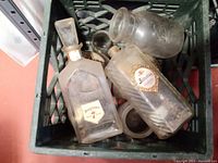 Top view of vintage glass bottles in a crate, showing rectangular bottles with liquor labels and other glass bottles with dirt and wear.
