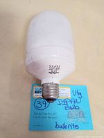 Close-up photo of the white Bulbrite CF16 light bulb with printed specifications including 130V 60Hz 16W and Made in Japan.